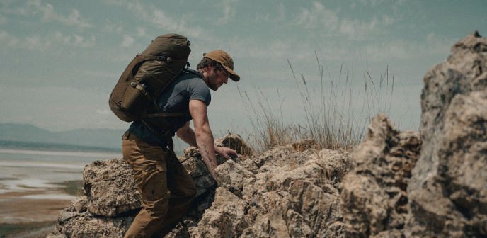 a man climbing rocks with a large tactical backpack