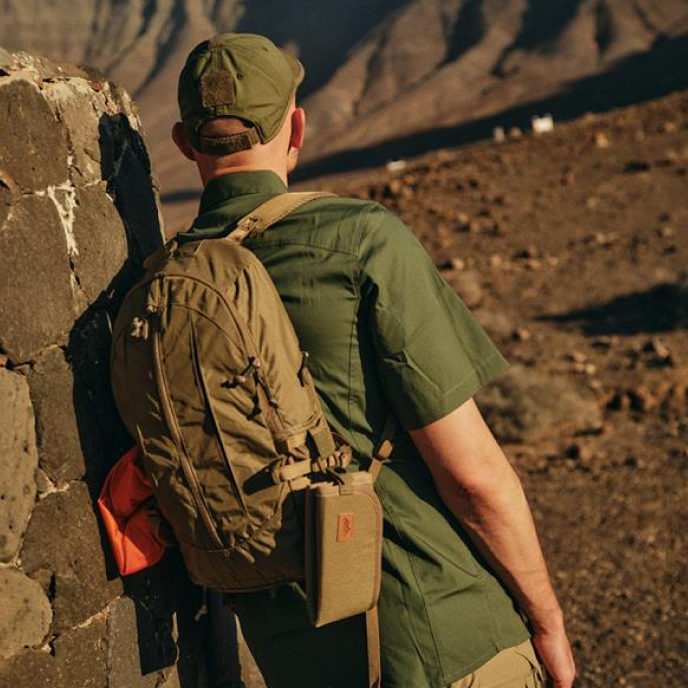 a man turned away, wearing a green shirt and carrying a tactical backpack for outdoor trips