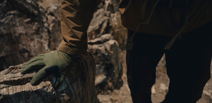 mężczyzna w zimowych rękawiczkach, opierający dłoń o skałę